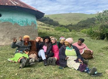 Professor Gail Super smiling and posing in front of a house, with hills behind